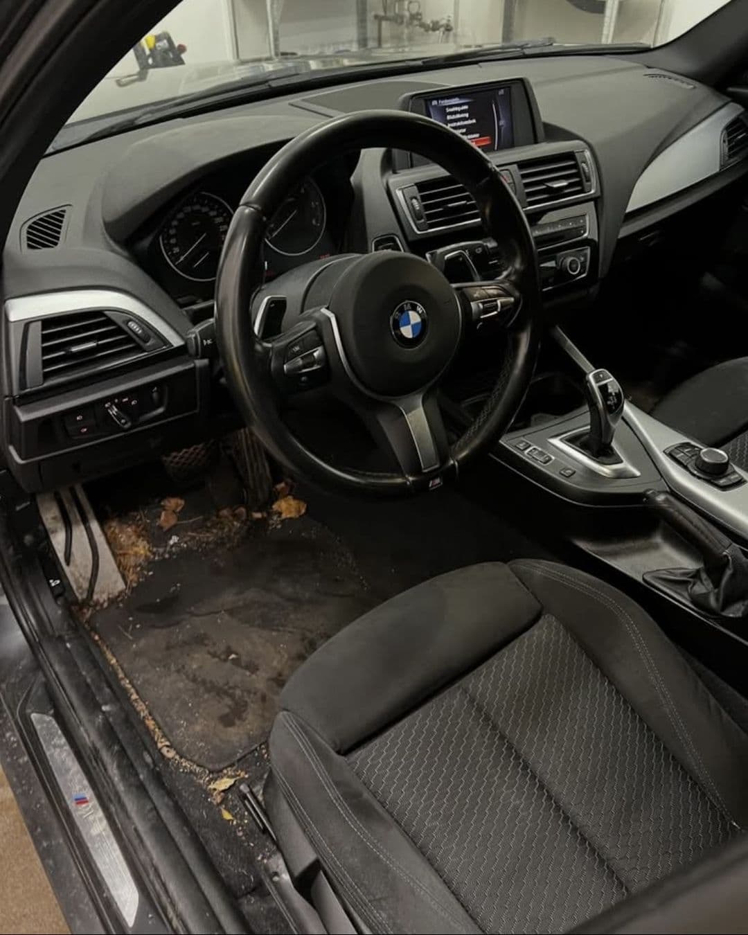 Smutsigt golv på förarsidan i en BMW 1-serie före rengöringen hos KOM-fort Bilvård i Örebro