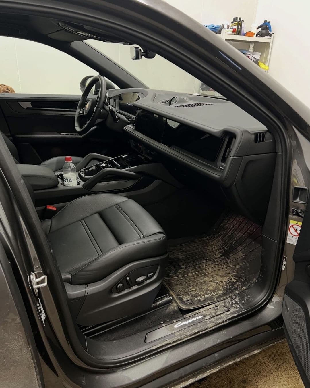 Passagerarplatsen i en Porsche Cayenne med smutsig golvmatta före rengöringen hos KOM-fort Bilvård i Örebro